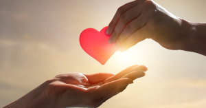 Hand passing paper heart to another person's hand