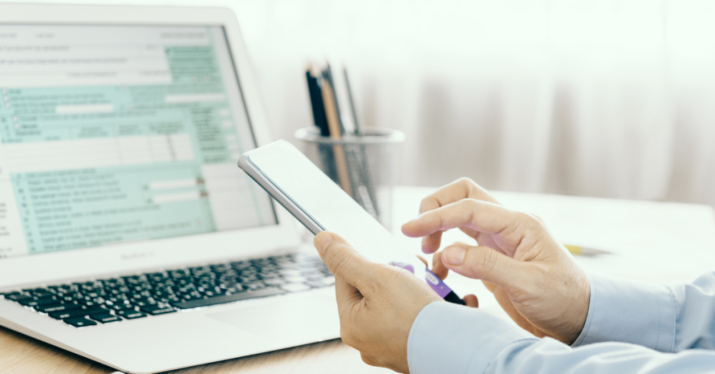 Man holding phone calculating back taxes on computer